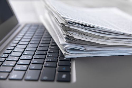 Stack of newspapers on a laptop representing hospitality news and press submissions