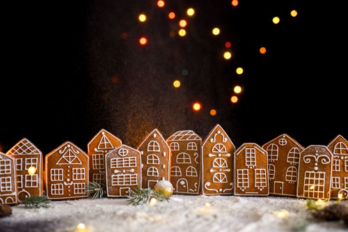 A quiet row of handcrafted gingerbread houses dusted with winter sugar, set against a dark backdrop with soft golden lights, evoking warmth, heritage and the silent transformation of small family hotels through the winter season.