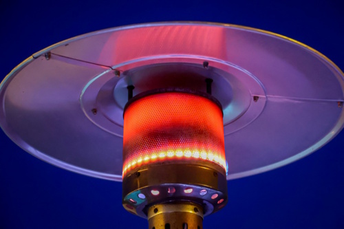 Close-up of a glowing outdoor patio heater against a dark sky, symbolizing the hospitality debate on heated terraces, climate impact, and sustainability.