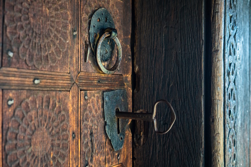 Old key in a traditional wooden door with ornate details, symbolizing the handover of a hospitality business.