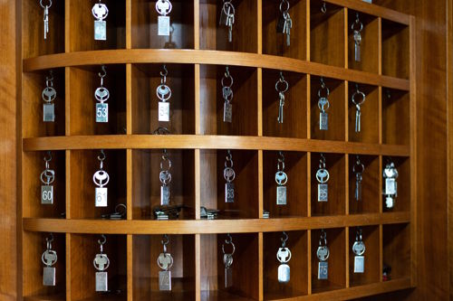 Vintage wooden hotel key rack with numbered keys hanging in open compartments, symbolizing aging hospitality infrastructure.