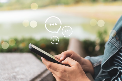 Close-up of a person holding a smartphone with chat icons floating above, symbolizing endless social media messages and unserious inquiries when selling a hospitality business.